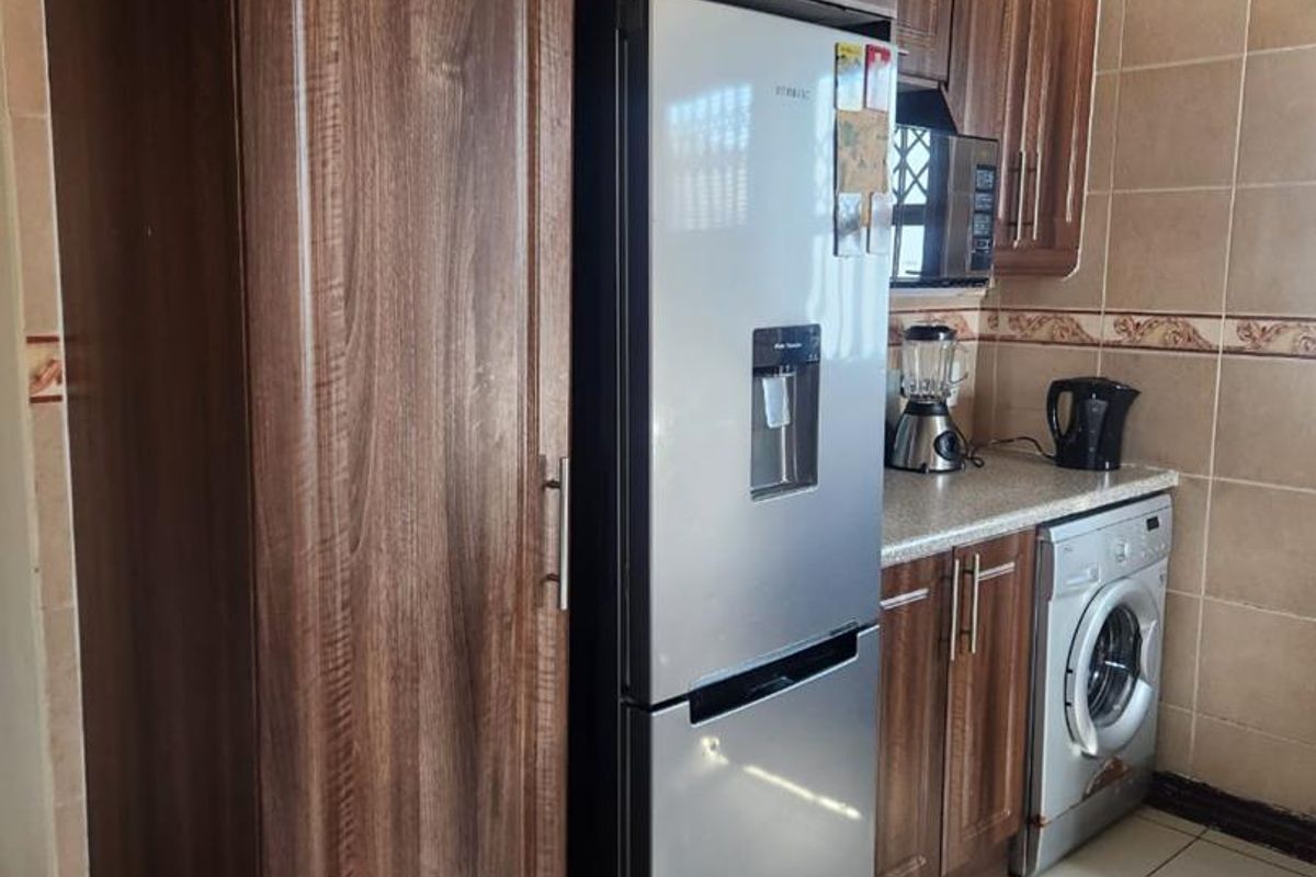 A functional kitchen featuring wood-grain cabinetry, tiled walls, and integrated space for a washing machine and refrigerator.
