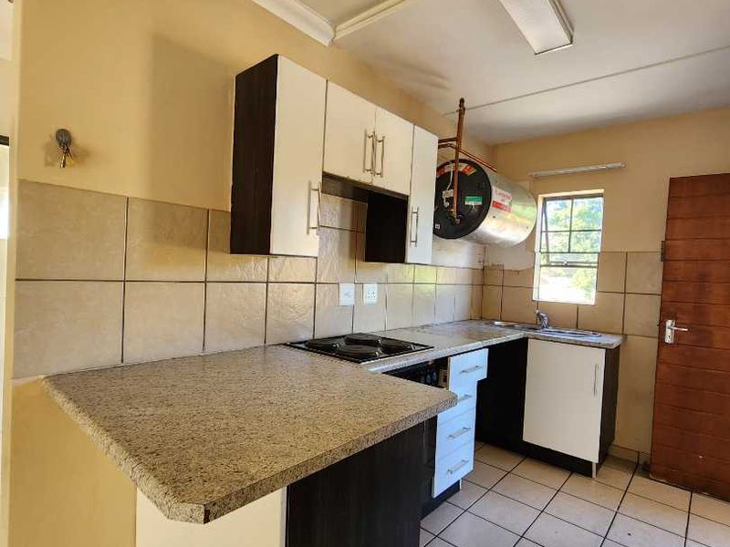 A functional kitchen featuring built-in cabinetry, granite countertops, an electric hob, and tiled flooring, offering a practical layout for daily use.