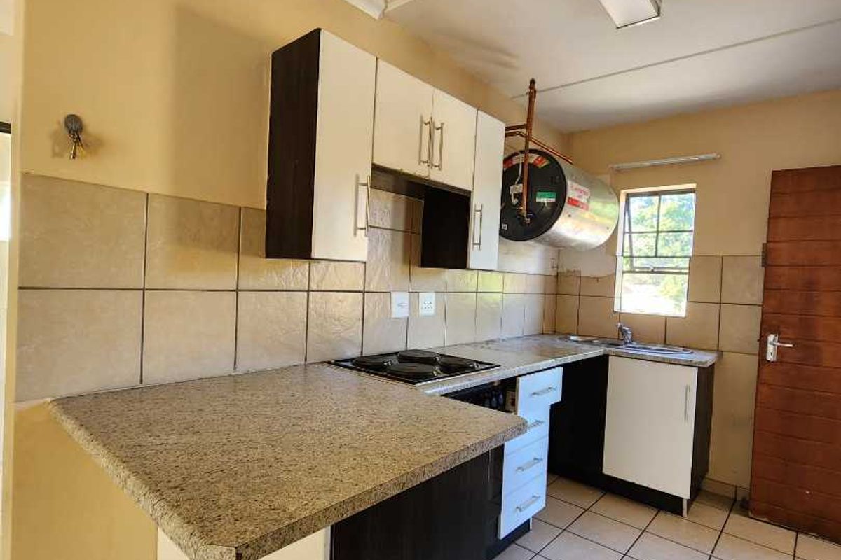 A functional kitchen featuring built-in cabinetry, granite countertops, an electric hob, and tiled flooring, offering a practical layout for daily use.