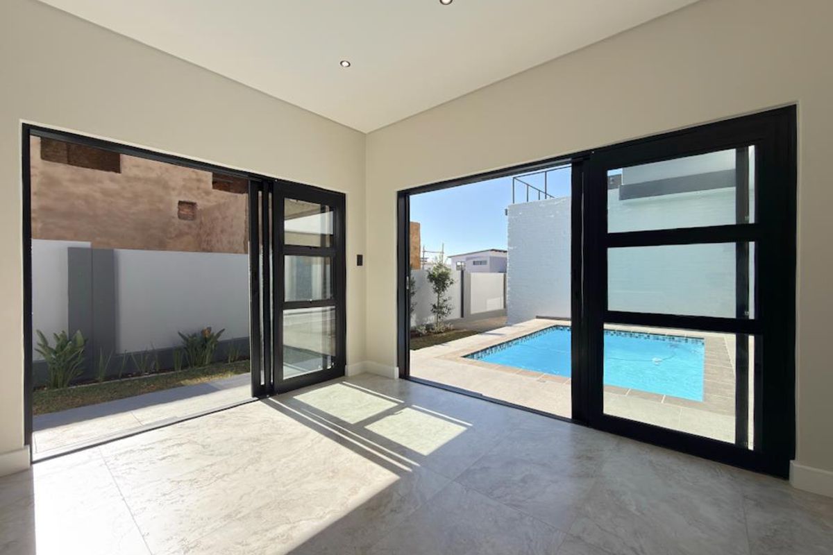 Bright living area featuring large black-framed sliding glass doors that open directly onto a private pool and patio area.