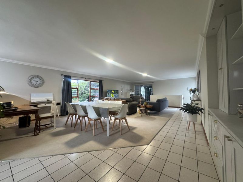 Spacious open-plan living and dining area featuring a combination of tiled and carpeted flooring, built-in cabinetry, and large windows providing natural light.