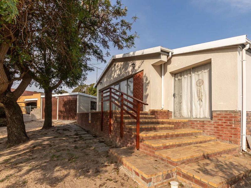 Rear exterior view of the house featuring a brick staircase with timber handrails, sliding glass doors, and a detached garage in the background.