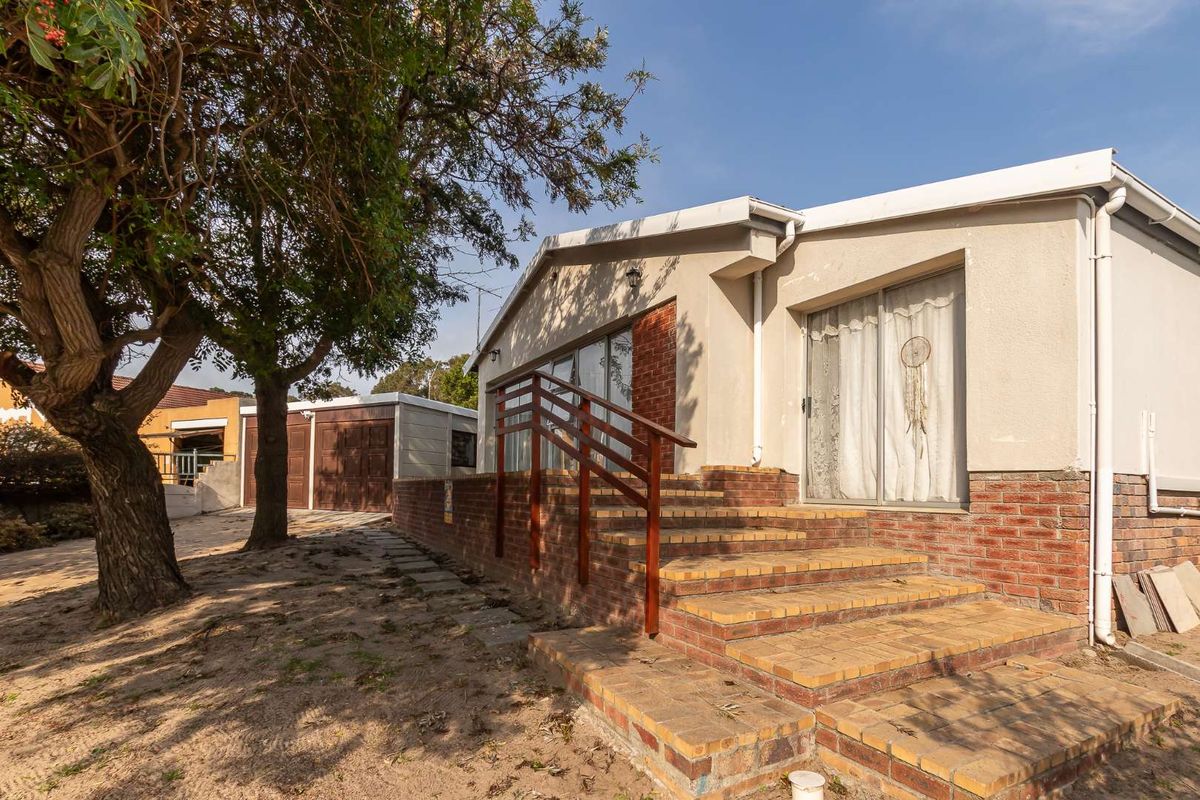 Rear exterior view of the house featuring a brick staircase with timber handrails, sliding glass doors, and a detached garage in the background.