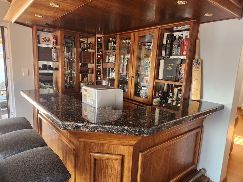 A well-maintained built-in wooden bar area featuring a granite countertop, glass display cabinets, and integrated lighting, perfect for entertaining.