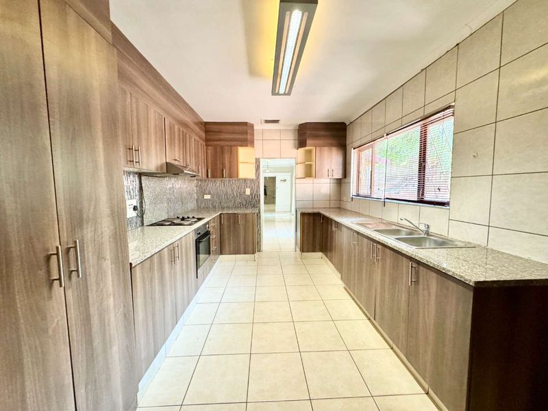 A spacious, well-maintained kitchen featuring wood-finish cabinetry, granite countertops, a double basin sink, and built-in cooking appliances with neutral tiled flooring.