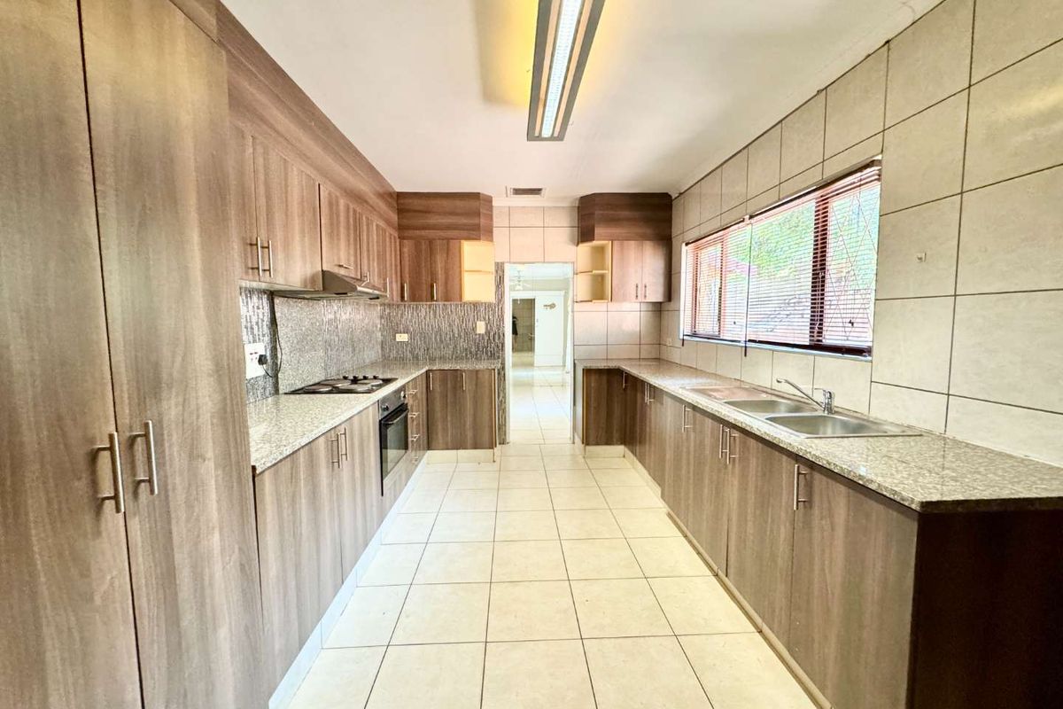A spacious, well-maintained kitchen featuring wood-finish cabinetry, granite countertops, a double basin sink, and built-in cooking appliances with neutral tiled flooring.
