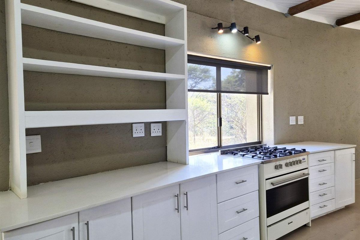 A clean, modern kitchen featuring white cabinetry, stone countertops, a gas stove with oven, and built-in shelving against a textured wall finish.