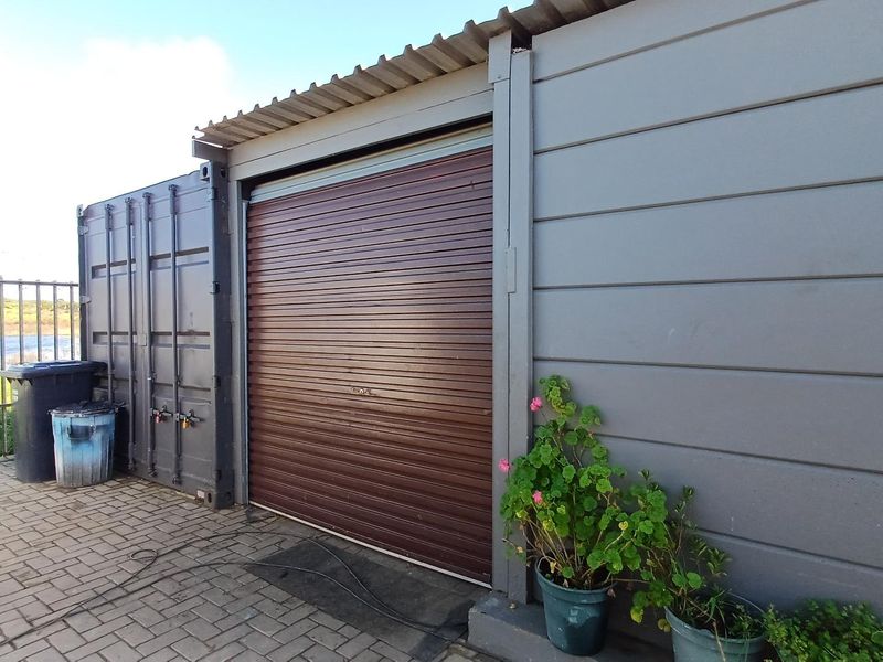 Industrial-style garage unit featuring a secure roller shutter door, metal cladding, and a durable corrugated roof, situated on a paved exterior area.