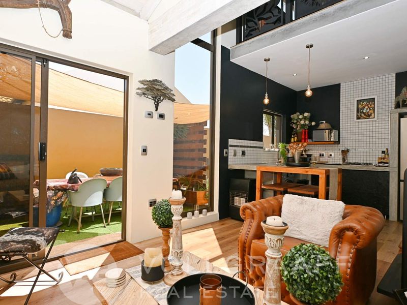 Modern open-plan living area featuring high ceilings, exposed beams, and a seamless transition to an outdoor patio through large sliding glass doors.