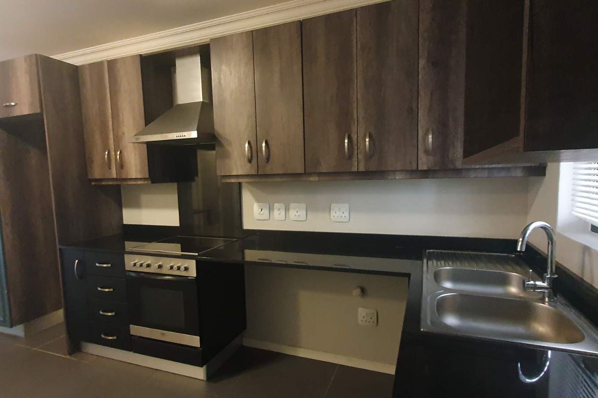 Modern kitchen featuring dark wood cabinetry, black granite countertops, integrated stainless steel appliances, and a double bowl sink with tiled flooring.