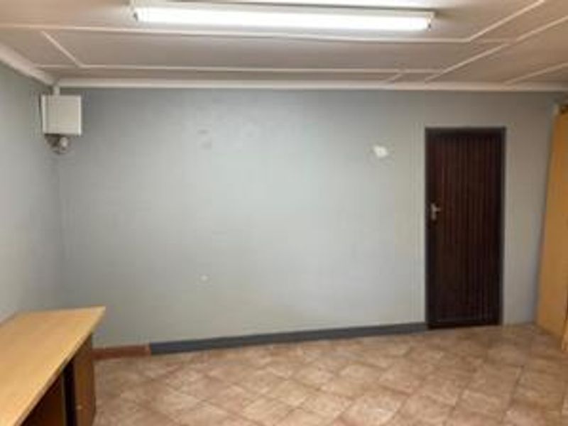 An empty office space featuring tiled flooring, a fluorescent ceiling light, and a single internal door, suitable for a variety of commercial uses.