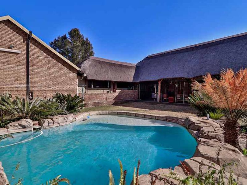 A well-maintained outdoor pool area featuring a rock-edged swimming pool, a covered patio space, and a traditional thatched roof structure.