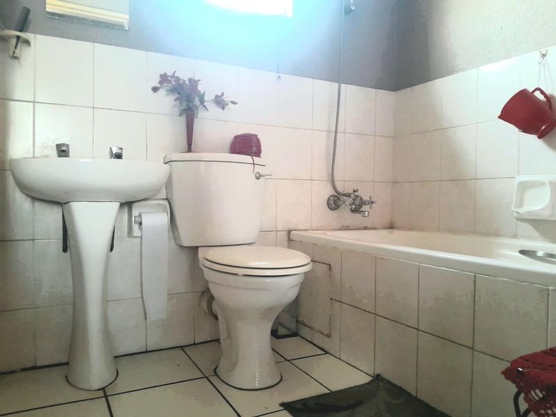 A functional bathroom featuring a pedestal basin, toilet, and bathtub with shower mixer, finished with white ceramic wall and floor tiles.