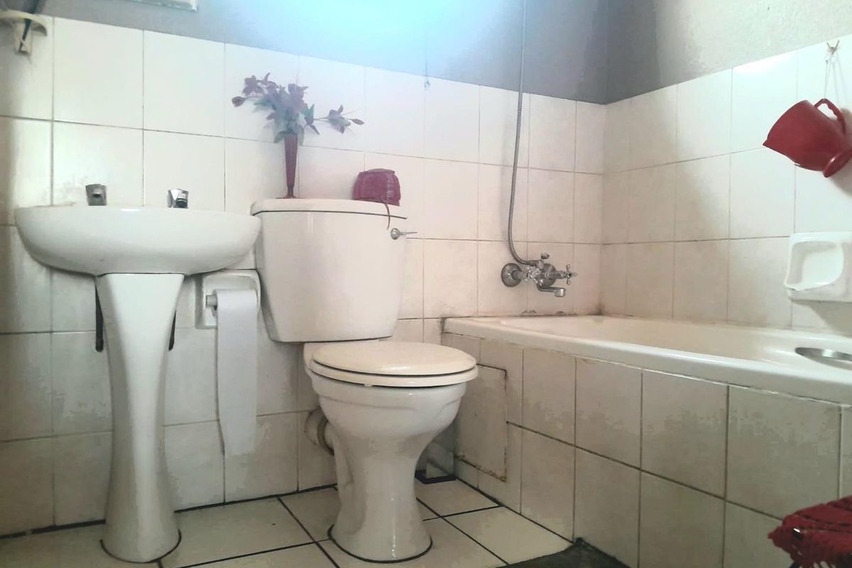 A functional bathroom featuring a pedestal basin, toilet, and bathtub with shower mixer, finished with white ceramic wall and floor tiles.