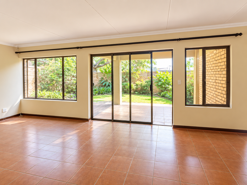 Spacious, sunlit living area featuring neutral walls, terracotta-style floor tiles, and large sliding glass doors providing seamless access to the rear patio and garden.