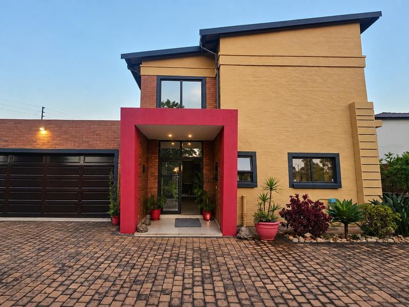 Modern double-story home featuring a striking red entrance portico, brick and rendered facade, paved driveway, and an integrated double garage.