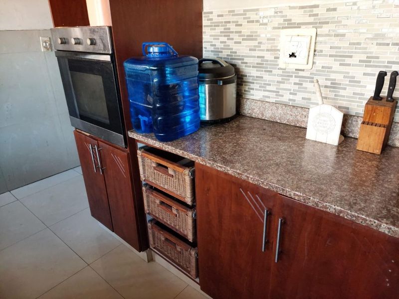 A kitchen area featuring timber cabinetry, laminate countertops, a built-in oven, and a mosaic tile backsplash with a damaged electrical outlet.