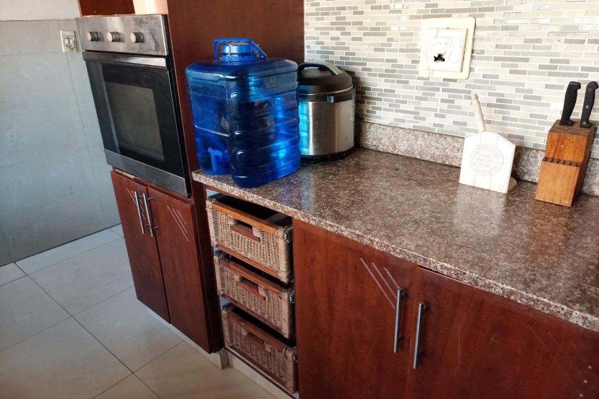 A kitchen area featuring timber cabinetry, laminate countertops, a built-in oven, and a mosaic tile backsplash with a damaged electrical outlet.