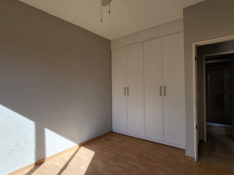 A bright, empty bedroom featuring neutral walls, laminate flooring, and ample built-in cupboard storage space.