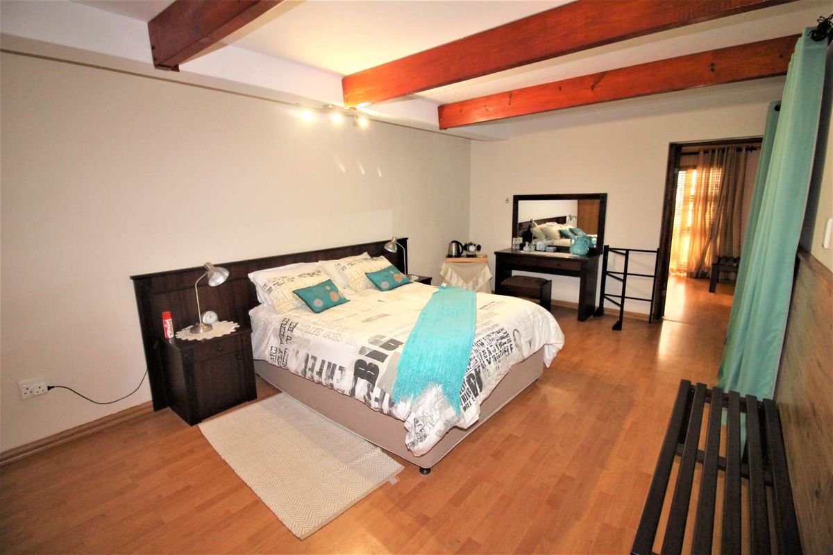 A spacious bedroom featuring exposed wooden ceiling beams, laminate flooring, and a built-in headboard, offering a warm and functional living space.