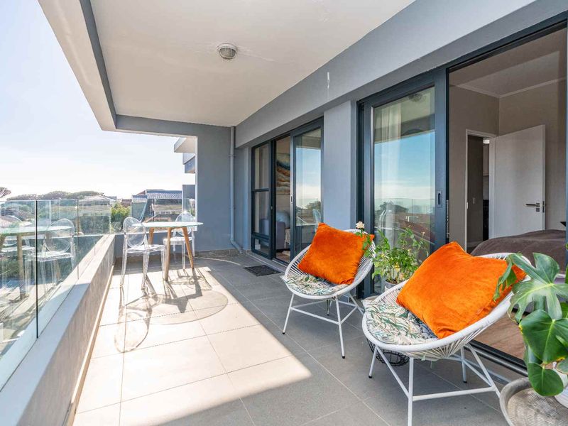A spacious covered balcony featuring modern tiled flooring, a sleek glass balustrade, and large sliding glass doors providing seamless indoor-outdoor flow.