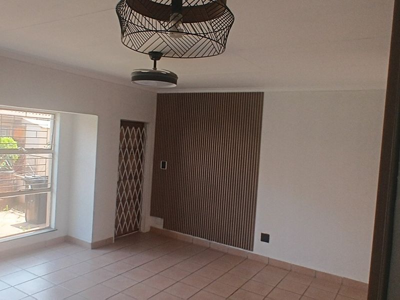A bright, empty living area featuring tiled flooring, a decorative slatted wood feature wall, a ceiling fan, and a security gate leading outdoors.