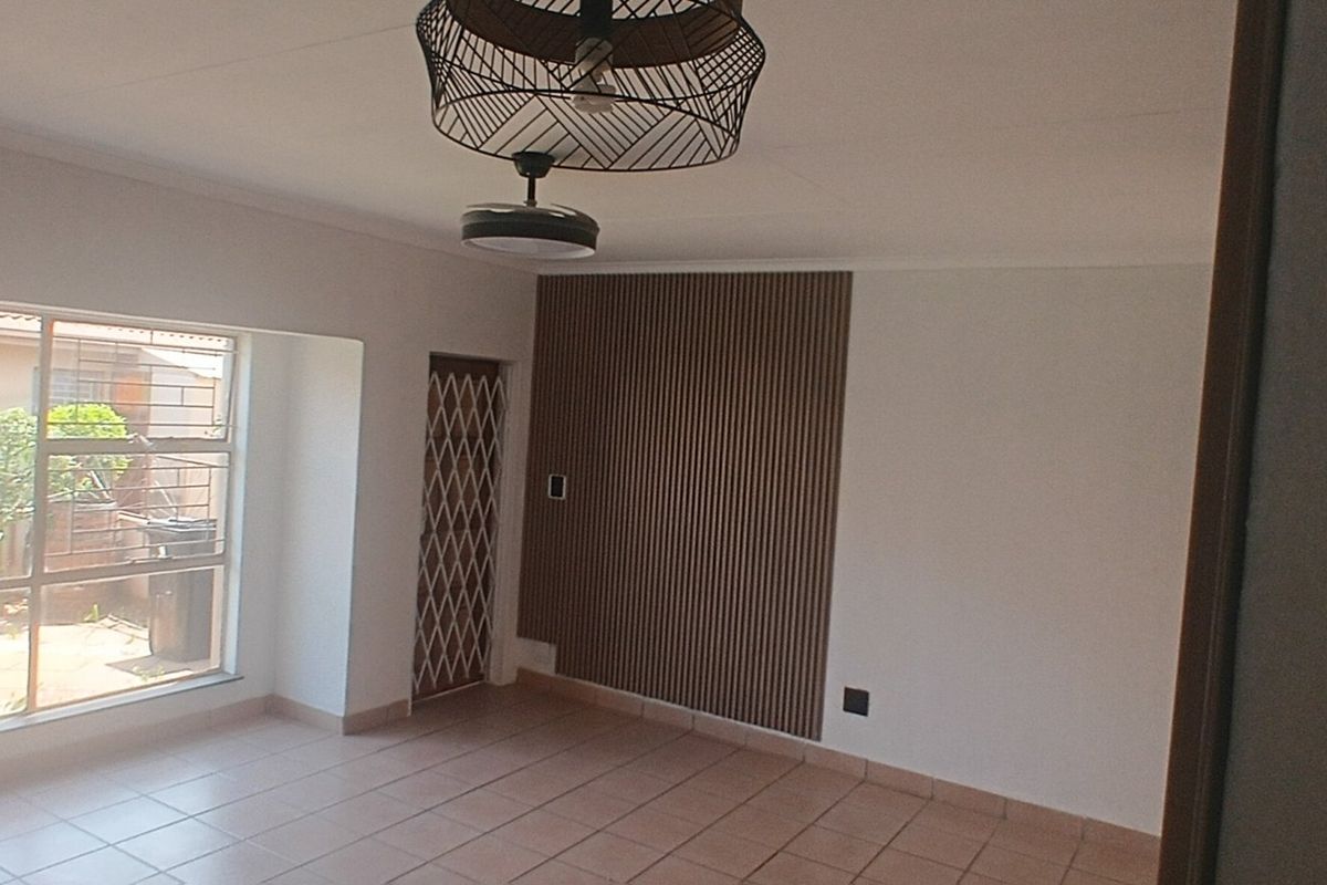 A bright, empty living area featuring tiled flooring, a decorative slatted wood feature wall, a ceiling fan, and a security gate leading outdoors.