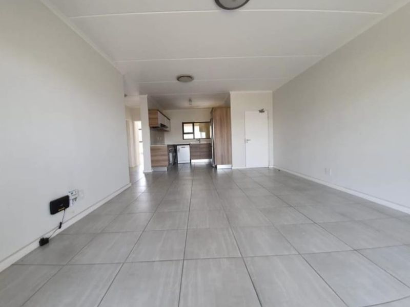 An open-plan living and kitchen area featuring neutral tiled flooring, modern cabinetry, and a functional layout, presented in a clean, vacant condition.