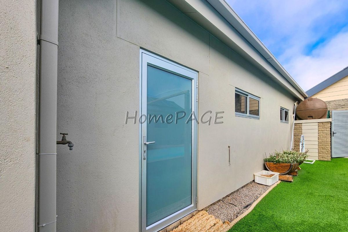 Exterior view of the rear building facade featuring a modern glass door, external water tap, and low-maintenance artificial lawn area.