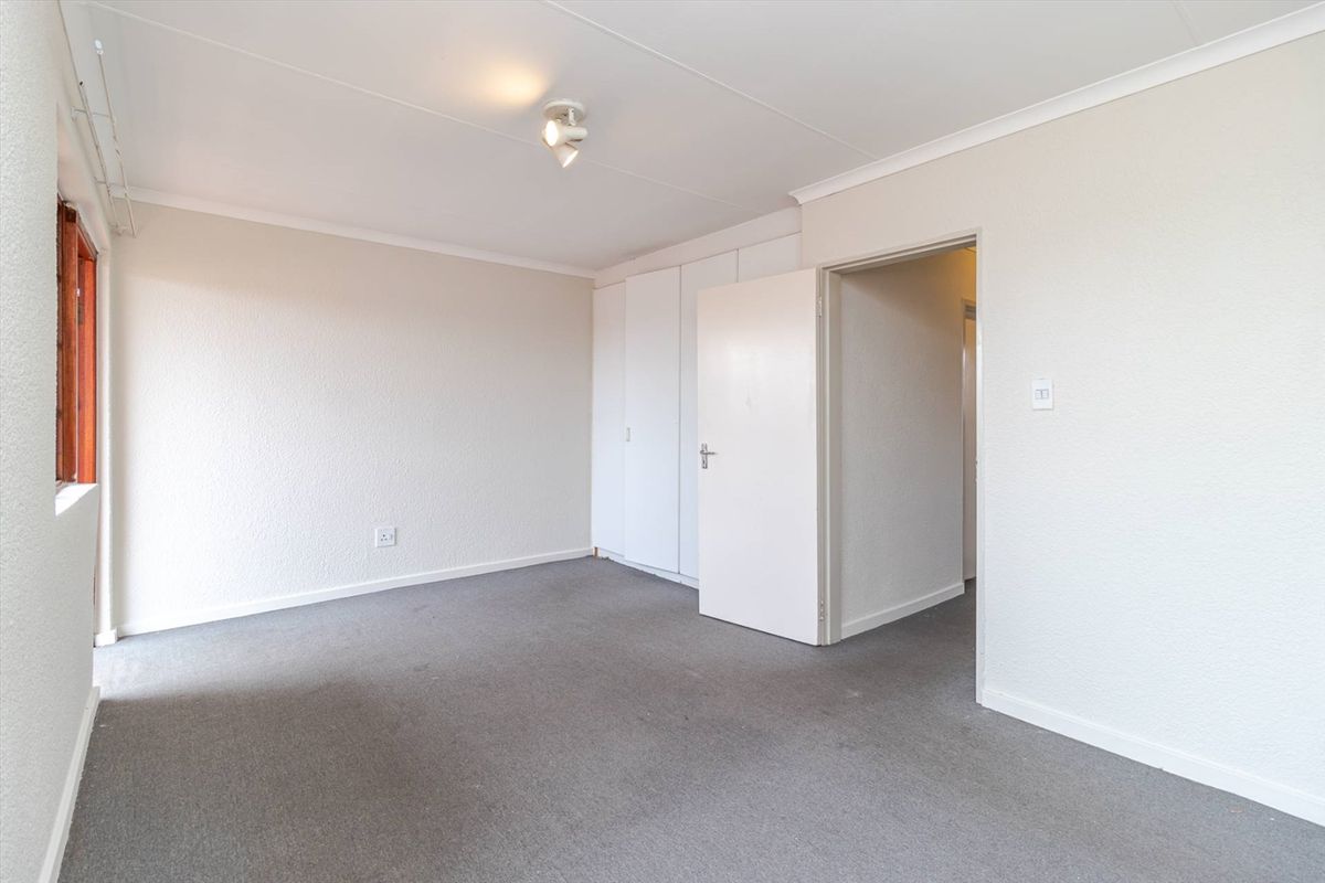 A bright, empty bedroom featuring neutral walls, grey carpeting, and built-in storage cupboards.