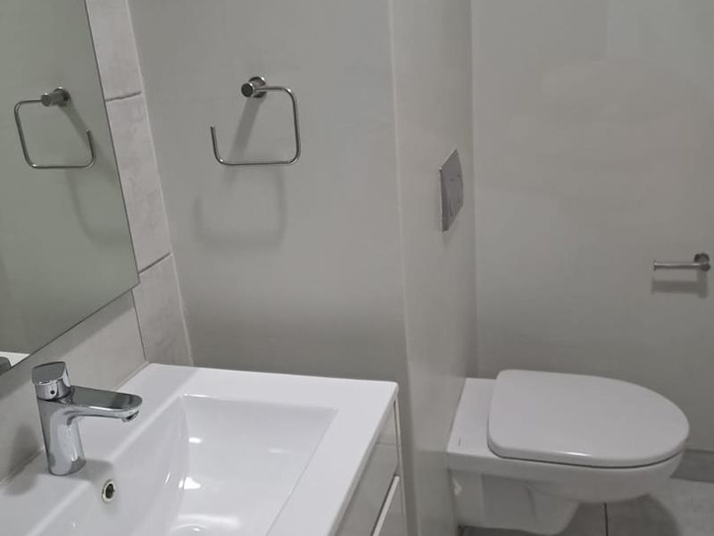 Modern bathroom featuring a wall-mounted toilet, vanity basin with chrome mixer tap, and neutral tiled flooring.