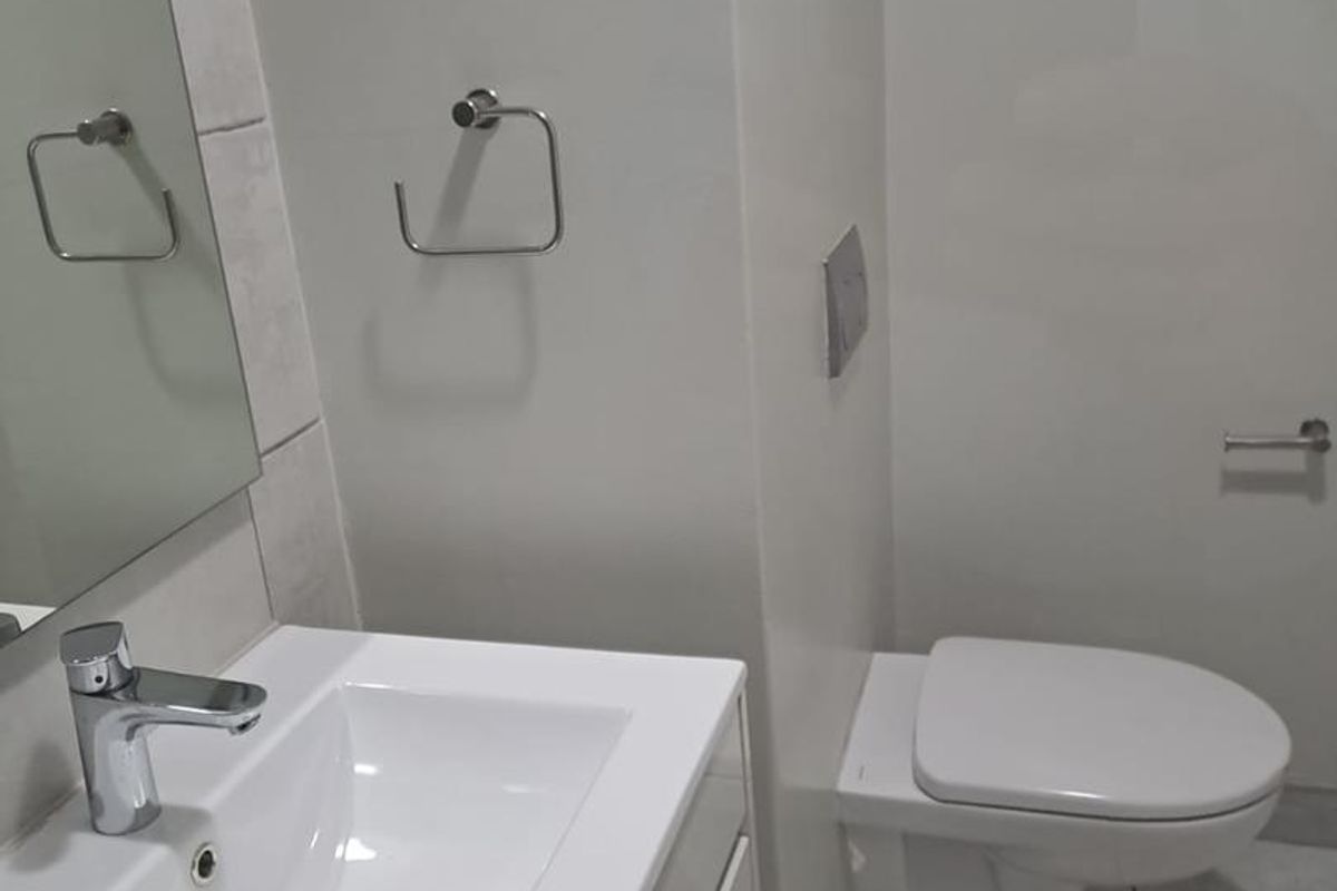 Modern bathroom featuring a wall-mounted toilet, vanity basin with chrome mixer tap, and neutral tiled flooring.
