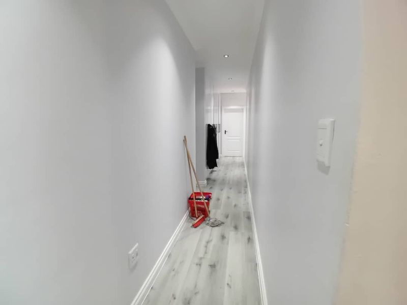 A clean, well-lit hallway featuring modern light-toned laminate flooring, recessed ceiling downlights, and neutral wall finishes.