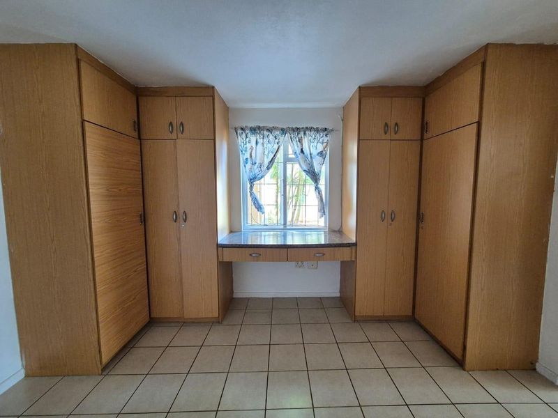 A bedroom featuring extensive built-in wooden cabinetry and a central built-in desk area beneath a window with security bars and tiled flooring.
