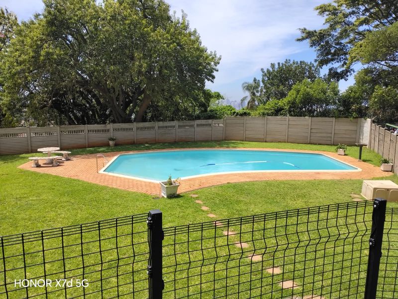 A well-maintained outdoor pool area featuring a swimming pool with paved surround, enclosed by a precast concrete wall and wire mesh fencing.