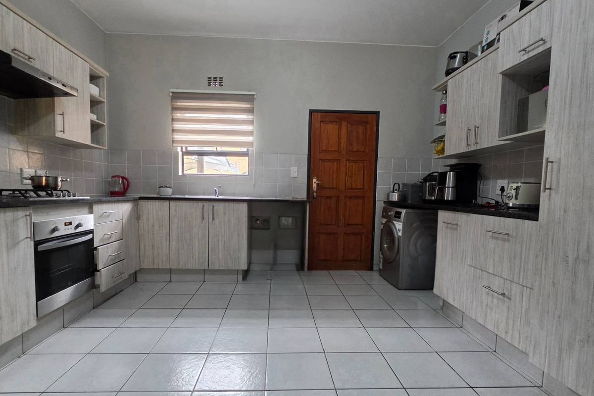 A functional kitchen featuring light wood-grain cabinetry, tiled flooring, a built-in oven, gas hob, extractor fan, and dedicated space for laundry appliances.