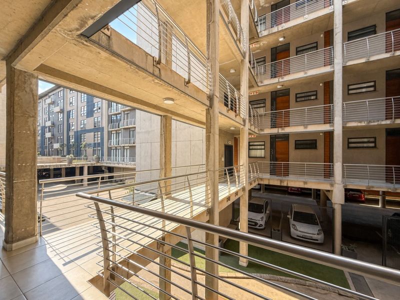 An elevated view of an apartment complex featuring open-air concrete walkways, metal railings, and covered parking areas within the building structure.