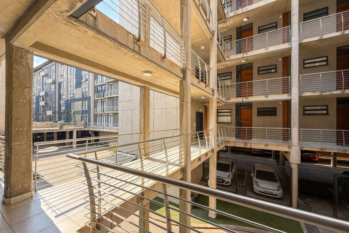 An elevated view of an apartment complex featuring open-air concrete walkways, metal railings, and covered parking areas within the building structure.