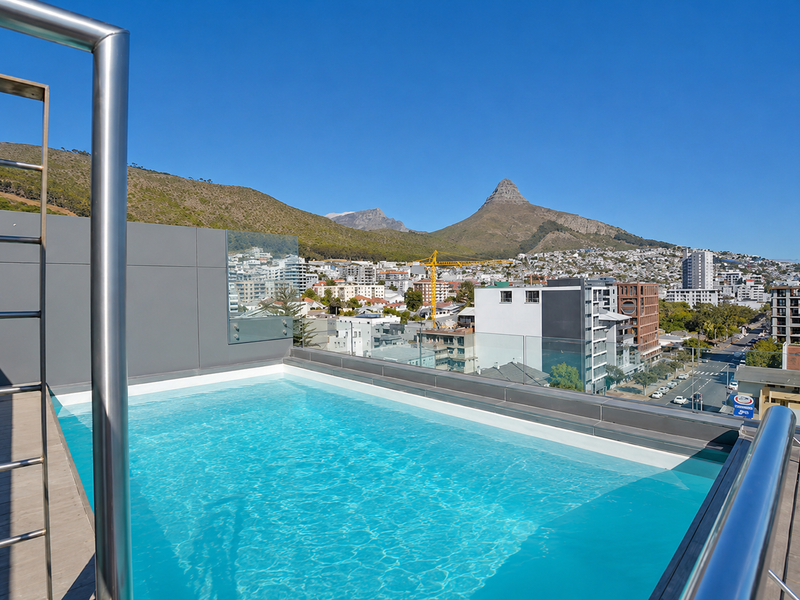 Rooftop swimming pool featuring a glass balustrade and stainless steel railings, offering panoramic mountain and city views.