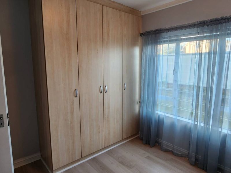 A bright bedroom featuring light wood-finish built-in cupboards and laminate flooring, offering a clean and neutral space.