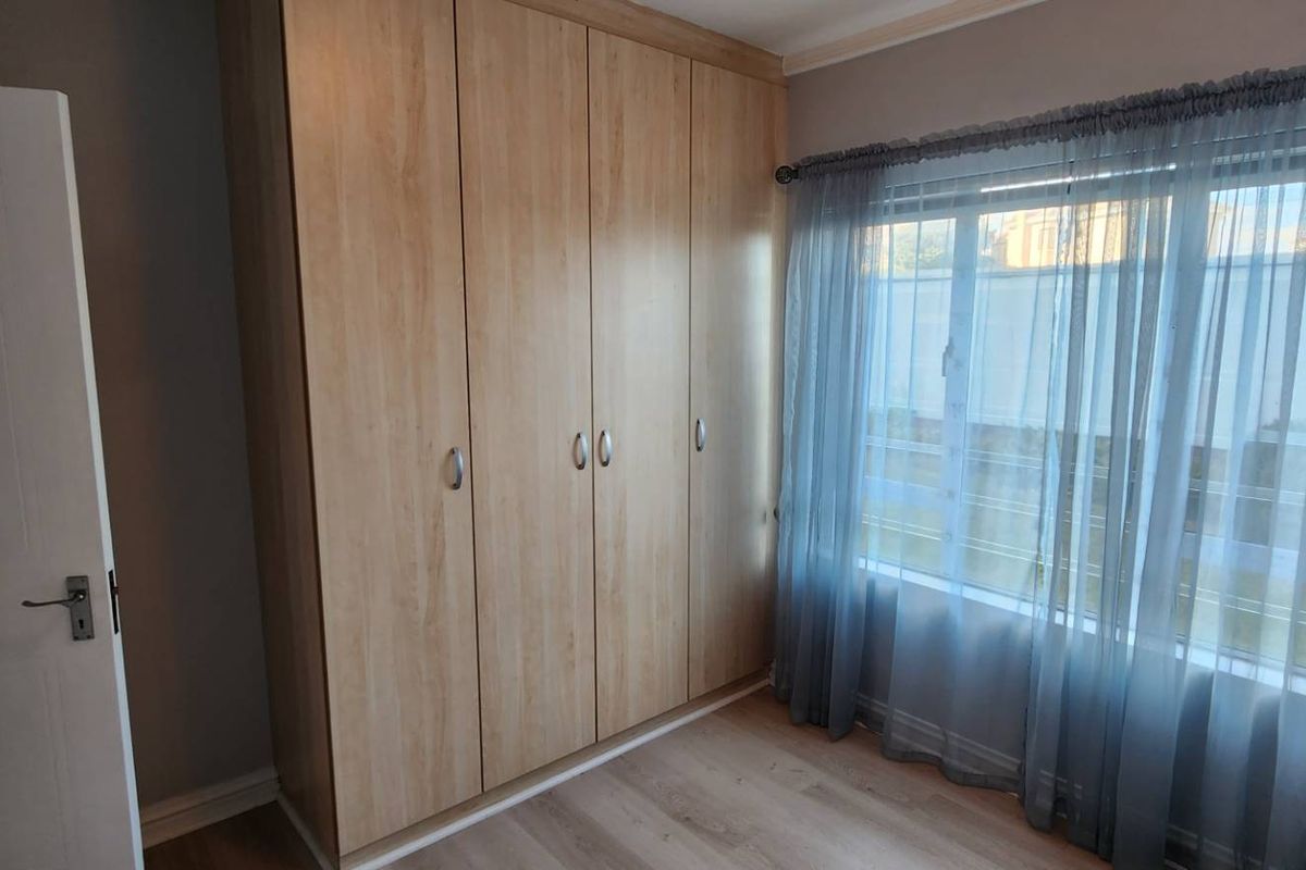 A bright bedroom featuring light wood-finish built-in cupboards and laminate flooring, offering a clean and neutral space.