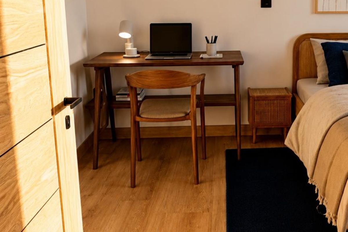 A well-lit bedroom featuring light wood flooring, a modern timber door, and a dedicated workspace area.