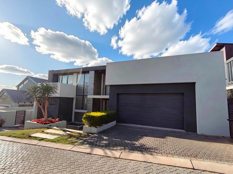 Modern contemporary house exterior featuring a double garage, stone-clad accents, large glass windows, and a neatly paved driveway.
