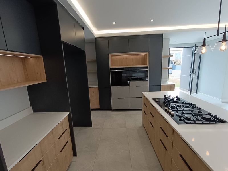 Modern kitchen featuring dark and wood-tone cabinetry, a central island with a gas hob, stone countertops, and integrated appliances.