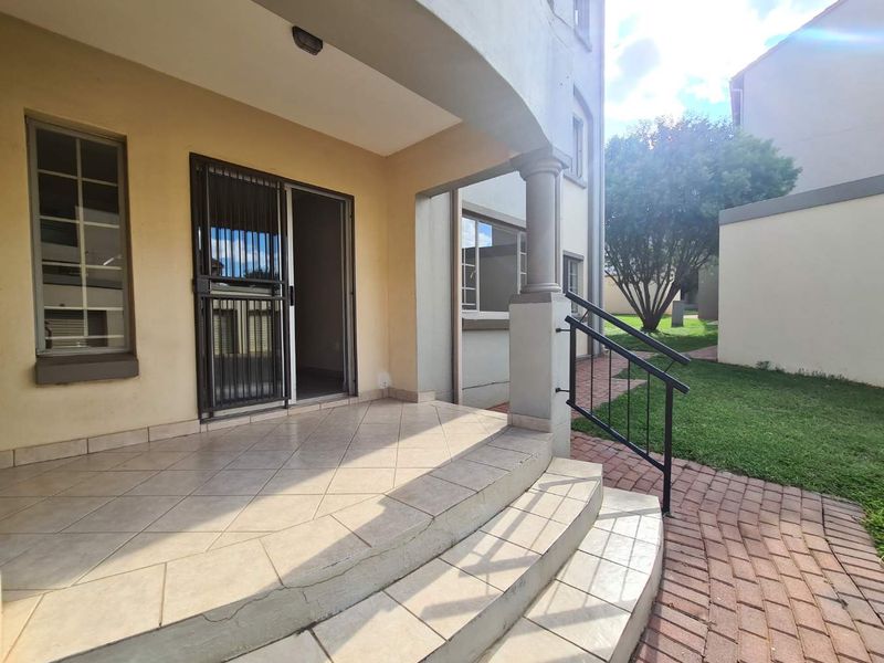 A covered patio area featuring tiled flooring, a security gate, and steps leading to a paved walkway and garden space.
