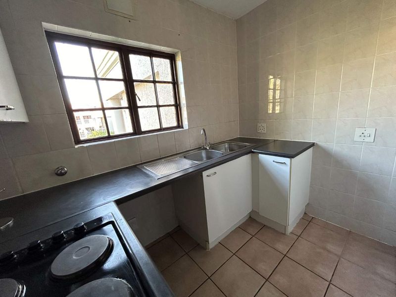 A functional kitchen featuring built-in cabinetry, laminate countertops, a stainless steel sink, and an electric hob with tiled splashbacks and flooring.