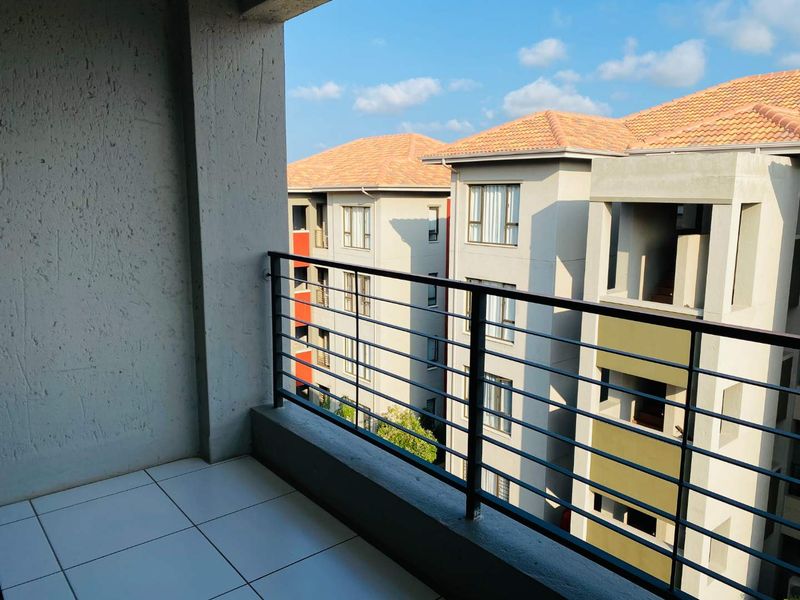 A covered balcony featuring tiled flooring and a metal balustrade, offering an elevated view of the surrounding apartment complex.