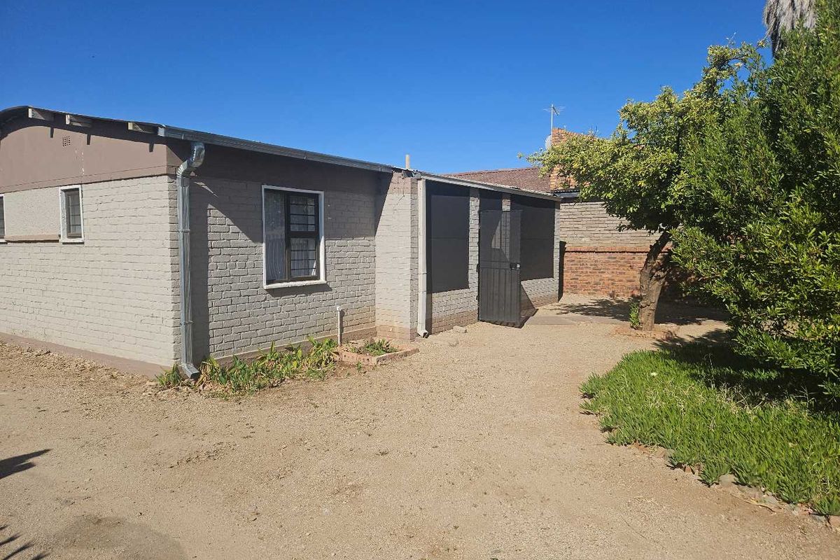 Rear exterior view of the property featuring a brick facade, security window bars, and a security gate leading to an unpaved backyard area.