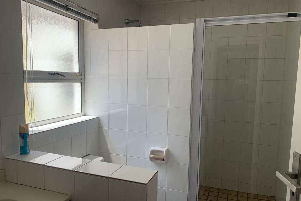 A functional bathroom featuring a tiled shower enclosure, a privacy wall, and a window for natural light.