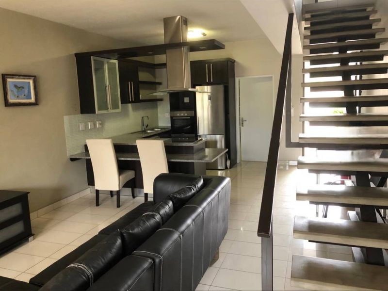 Open-plan living area featuring a modern kitchen with granite countertops, built-in appliances, and a striking staircase leading to the upper level.